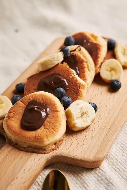 Pancakes with chocolate sauce, berries, and banana on a wooden plate