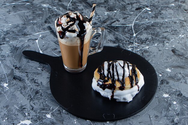 木の板にチョコレートのトッピングとコーヒーのグラスとパンケーキ。