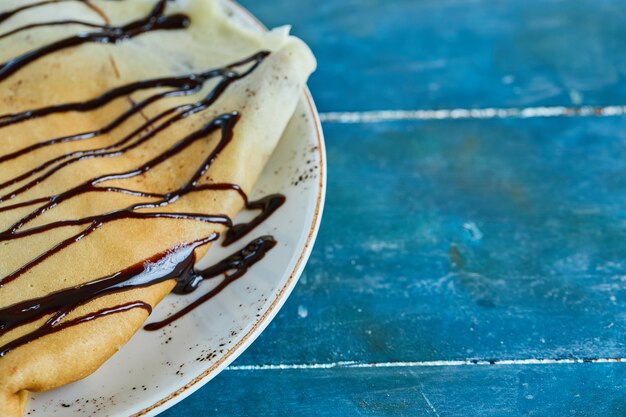 Pancakes with chocolate on the white plate in the blue surface