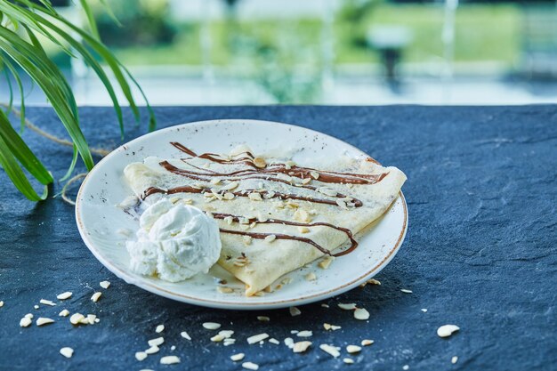 Pancakes with ice-cream, sprinkles, chocolate on the white plate in the dark surface