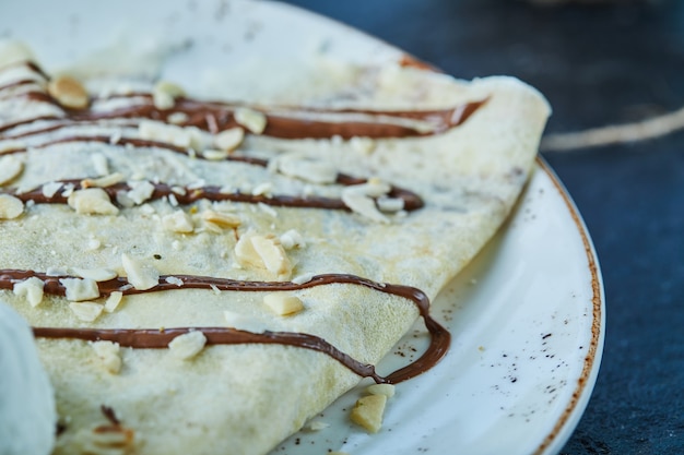 Pancakes with ice-cream, sprinkles, chocolate on the white plate in the dark surface