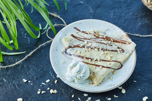 Pancakes with ice-cream, sprinkles, chocolate on the white plate in the dark surface