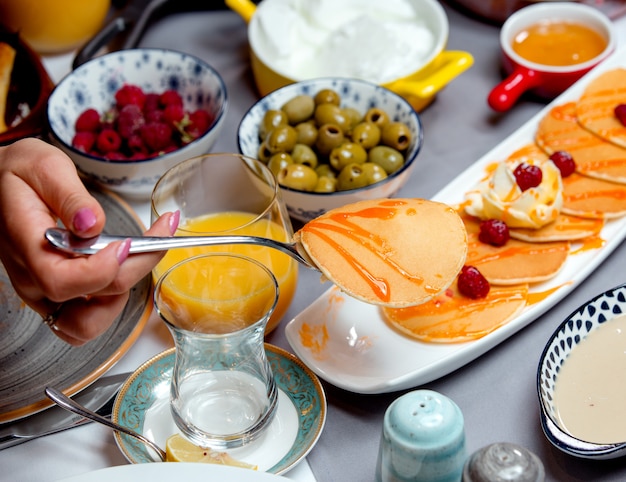 Pancakes with jam, olives, a glass of juice and raspberries