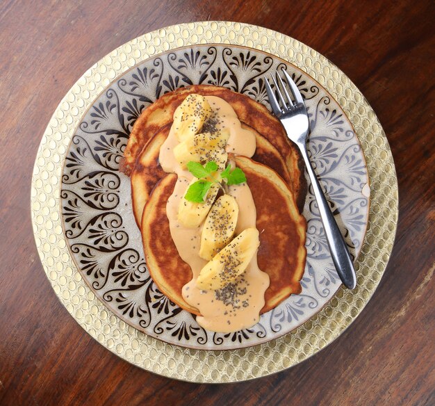 Pancakes with souse, bananas and chia seeds served on a plate with patterns