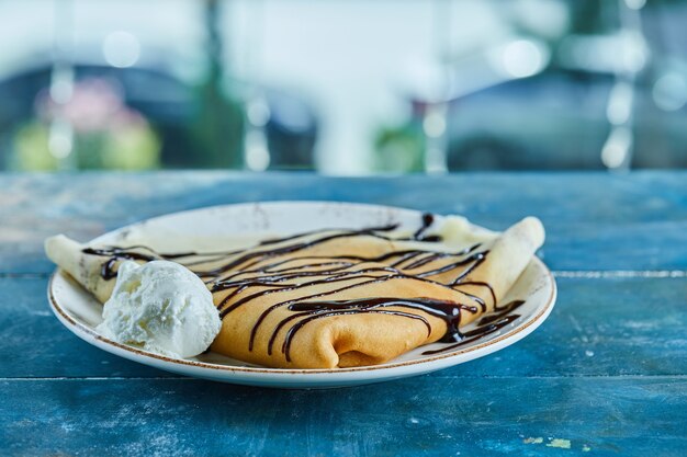 青い表面の白いプレートにバニラアイスクリーム、チョコレートのパンケーキ