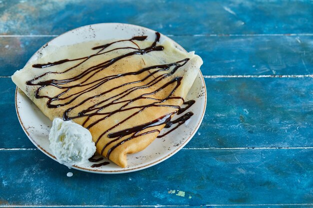 青い表面の白いプレートにバニラアイスクリーム、チョコレートのパンケーキ