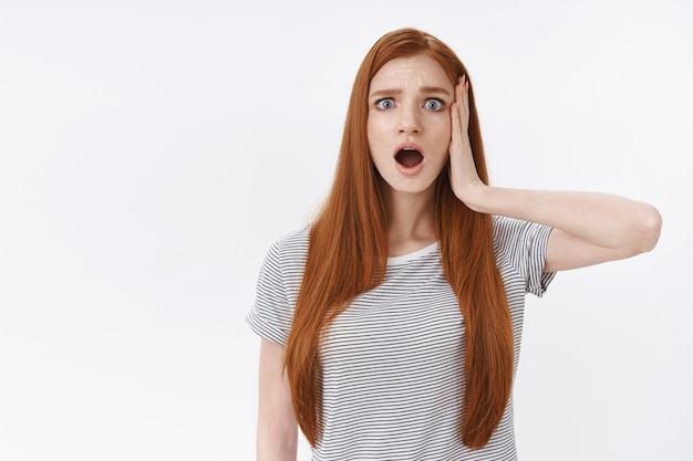 Free photo panicking shocked upset cute redhead european young girl frowning gasping open mouth disappointed touch head frustrated hear bad news standing displeased, white wall