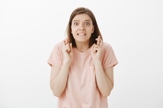 Panicking young woman student praying, hoping with fingers crossed, making wish or pleading