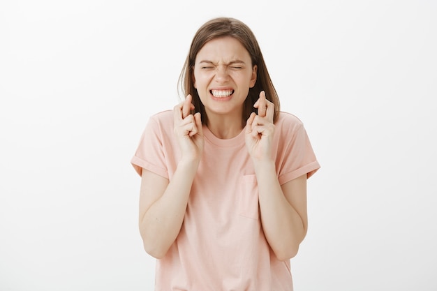 Panicking young woman student praying, hoping with fingers crossed, making wish or pleading