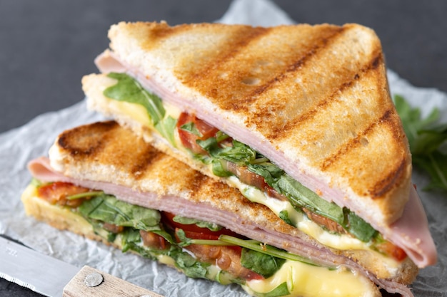 Panino panini con prosciutto, formaggio, pomodoro e rucola su fondo di ardesia nera