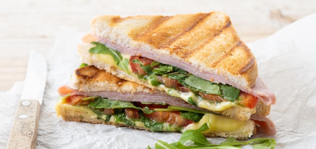 Panini sandwich with ham cheese tomato and arugula on wooden table