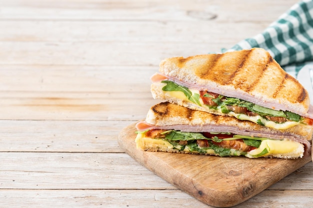 Foto gratuita panino panini con prosciutto, formaggio, pomodoro e rucola su tavolo di legno