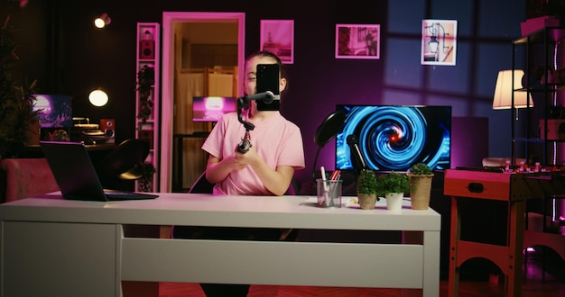 Foto gratuita panoramica di un giovane che filma un video con il telefono sul treppiede in un soggiorno rosa illuminato al neon