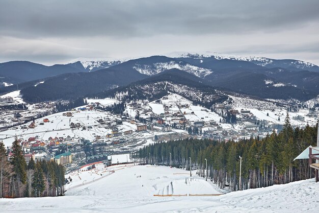 Панорама горнолыжного курорта, склон, люди на подъемнике, лыжники на трассе среди зеленых сосен и снежных копий. Копировать пространство