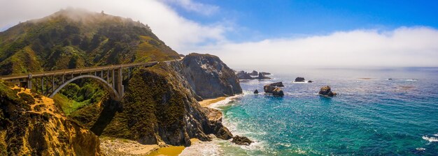 美しい青い水の近くの緑の丘にあるカリフォルニアビクスビー橋のパノラマ空中ショット