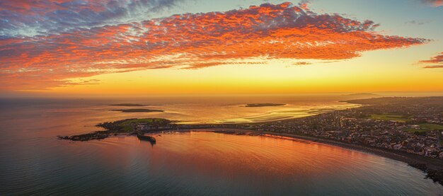 Panoramic aerial shot of land surrounded by the sea under an orange sky at sunset
