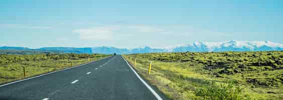 Foto gratuita panoramica di una lunga strada asfaltata circondata da campi erbosi in islanda