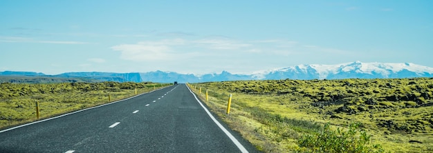 Panoramic of a long asphalt road surrounded by grassy fields in Iceland