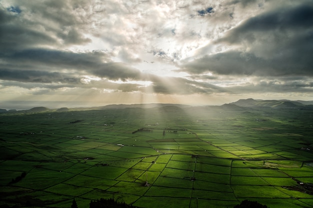 Panoramic shot of an agrucultural field with rays of sun shining through the clouds