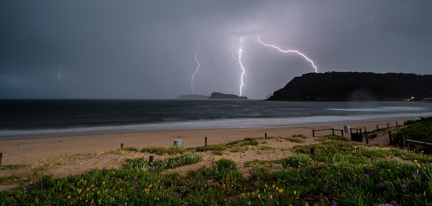 Panoramic shot of a beach surrounded by the sea and hills during the lightning in the evening