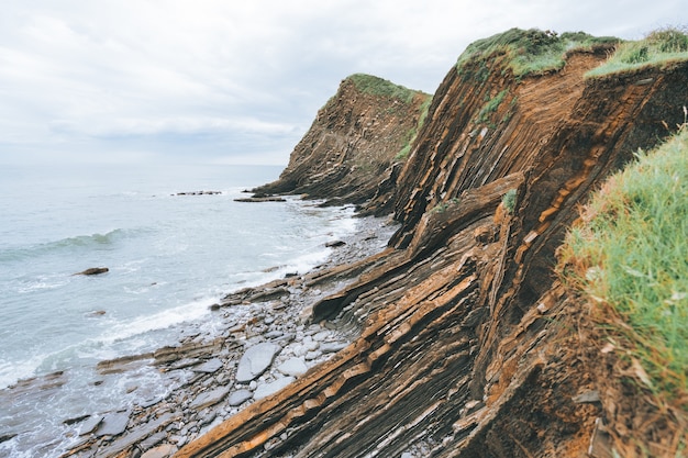 Free photo panoramic shot of cliffs filled with green grass next to the blue sea during daylight