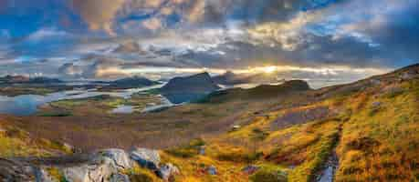 Foto gratuita colpo panoramico di colline erbose e montagne vicino all'acqua sotto un cielo nuvoloso blu in norvegia