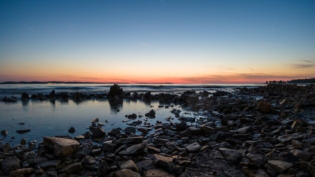 Panoramic shot of the rocky shore with a clear sky during sunrise