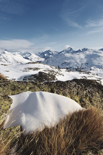 Panoramic shot of snow covered French alps with the sun shining under blue skies