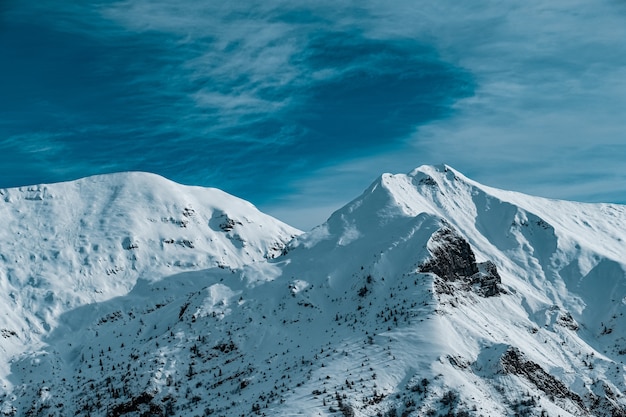Панорамный снимок заснеженных горных вершин под пасмурным голубым небом