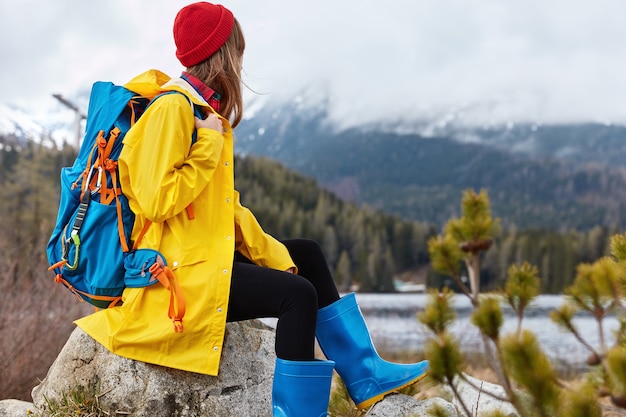 Panoramic view of active female tourist in raincoat poses on picturesque shore