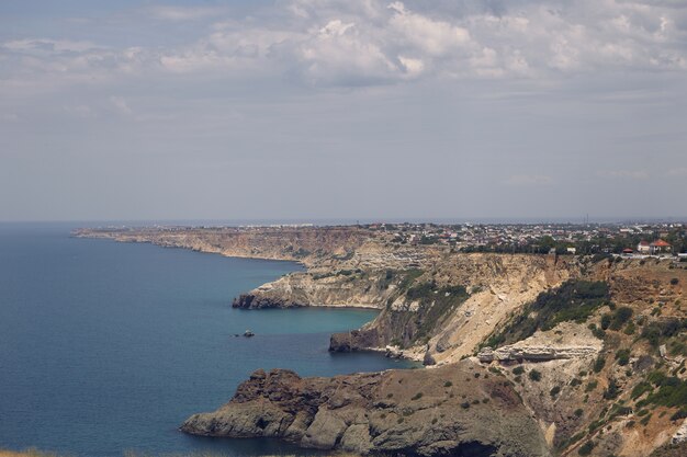 Panoramic view of craggy coastline with small towns by peaceful blue sea. Seascape and long rugged shore on cloudy summer day. Nature, seaside, vacations, holiday and tourist destintion concept