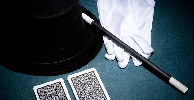 Panoramic view of playing card; white gloves; top hat and magic wand on green background