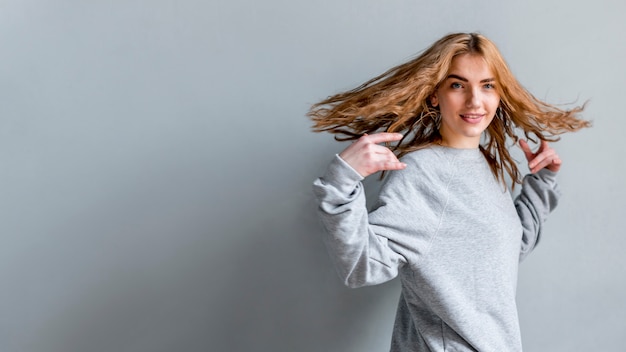 Foto gratuita vista panoramica dei capelli d'oscillazione sorridenti della giovane donna contro la parete grigia