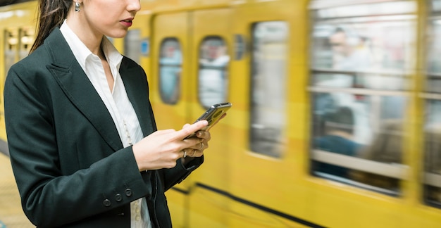 Panoramic view of young businesswoman using mobile phone standing near the subway train