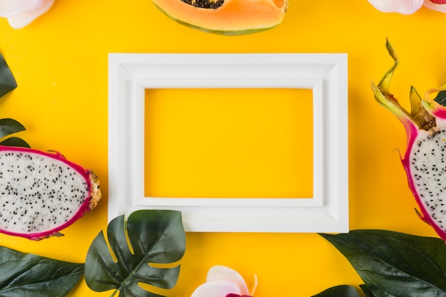 Papaya; dragon fruit; leaves around the empty white border frame against yellow backdrop