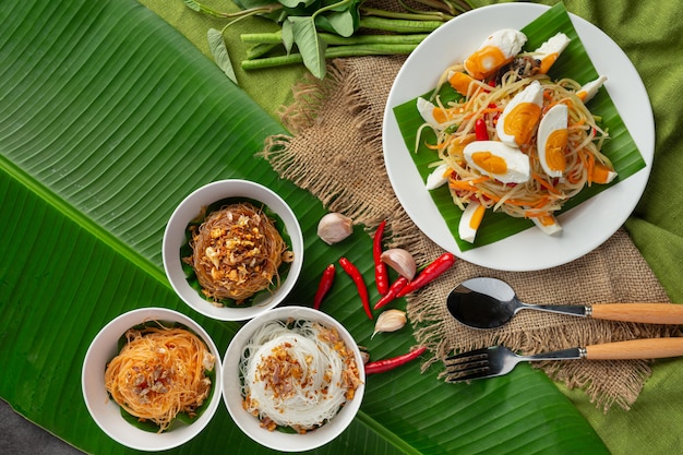 Салат из папайи, подается с рисовой лапшой и овощным салатом. Украшен ингредиентами тайской кухни.