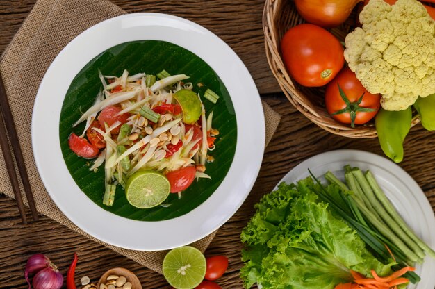 Papaya Salad (Som tum Thai) on a white plate on a wooden table.