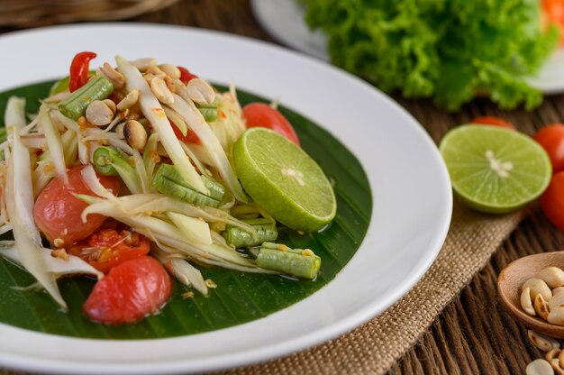 Papaya Salad (Som tum Thai) on a white plate on a wooden table.