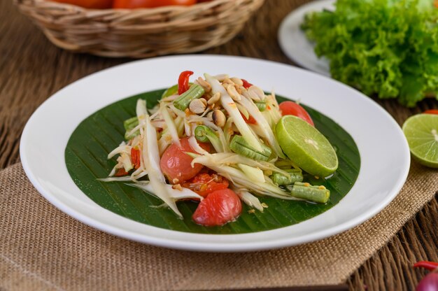 Papaya Salad (Som tum Thai) on a white plate on a wooden table.