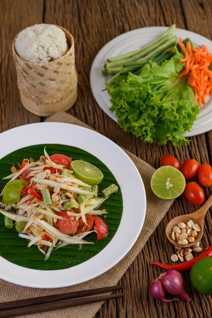 Салат из папайи (Som tum Thai) на белой плите на деревянном столе.
