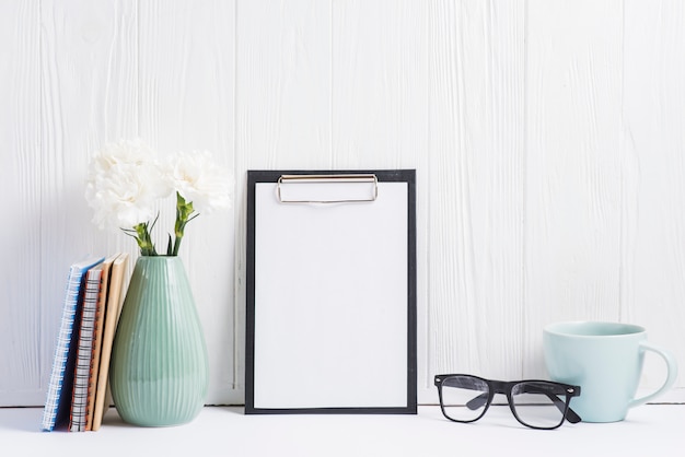 Paper on clipboard; vase; eyeglasses; cup; books and vase on white backdrop