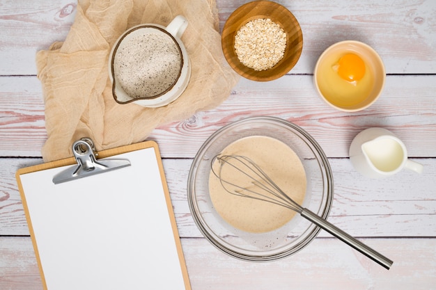 Paper on clipboard with flour; egg yolk; milk and oat bran on wooden table