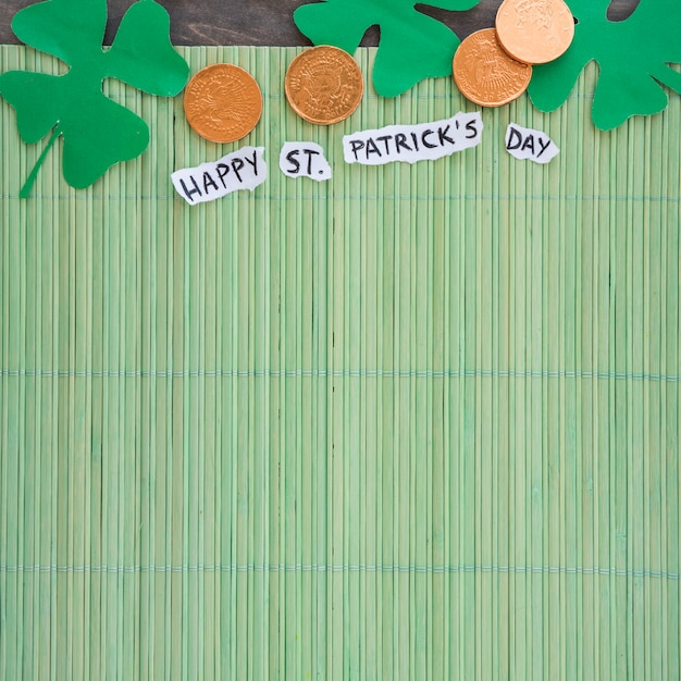 コインと竹マットの上の幸せなSt Patricks日タイトルの近くの紙クローバー