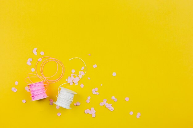 Paper confetti with pink and white spool on yellow backdrop