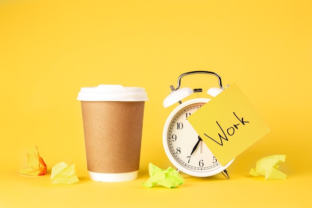 Free photo paper cup and alarm clock with paper reminder on yellow background isolated