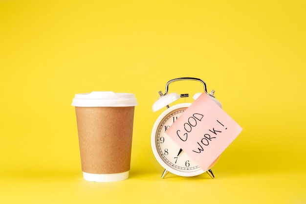 Free photo paper cup and alarm clock with paper reminder on yellow background isolated