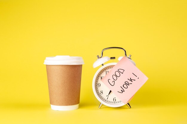 Paper cup and alarm clock with paper reminder on yellow background isolated