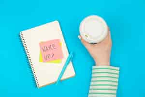 Free photo paper cup and notebook with paper reminder with text wake up top view