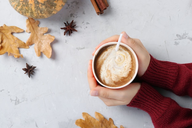 Paper cup with delicious pumpkin latte with spices in female hands on a gray table