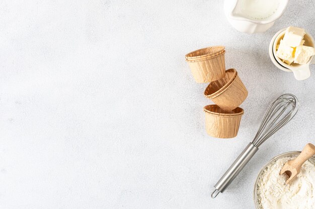 흰색 콘크리트 배경에 있는 종이 컵케이크 베이킹 팬과 재료 밀가루 버터 설탕 털 우유 복사 공간 탑 뷰 베이킹 컨셉 플랫 레이
